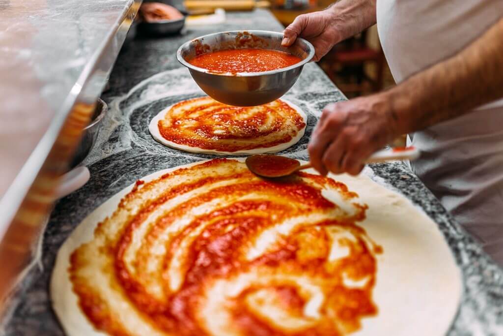 Man putting sauce on pizza dough