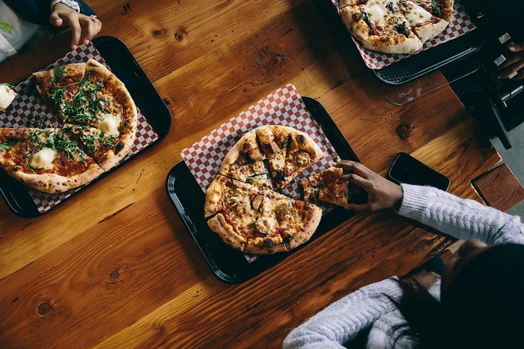 Group of people eating pizzas on a wooden table