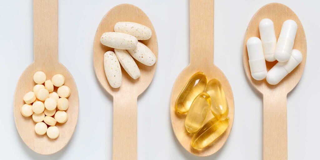 Wooden spoons holding different kinds of vitamins and supplements