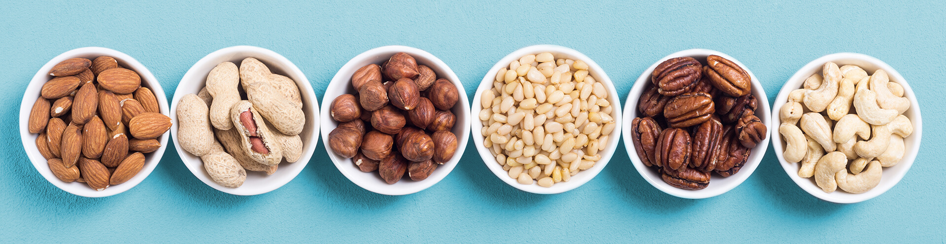 Mixed nuts in small white bowls against a blue background