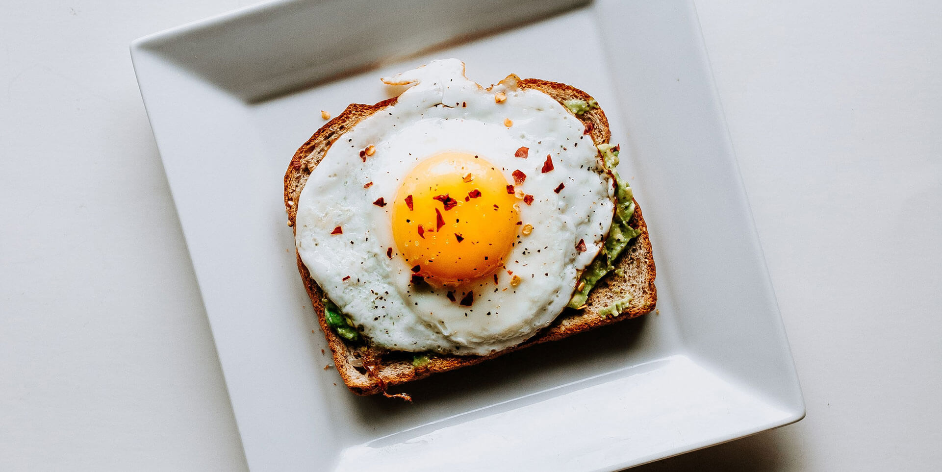 Avocado toast with fried egg on a square, white plate