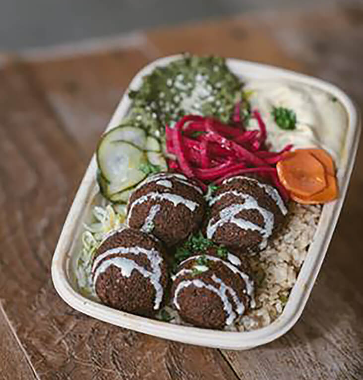 Four Falafels on a bed of rice (VE, GF) Chickpea dumpling, garlic, onion, cilantro, parsley all in a rectangular cream paper tray.